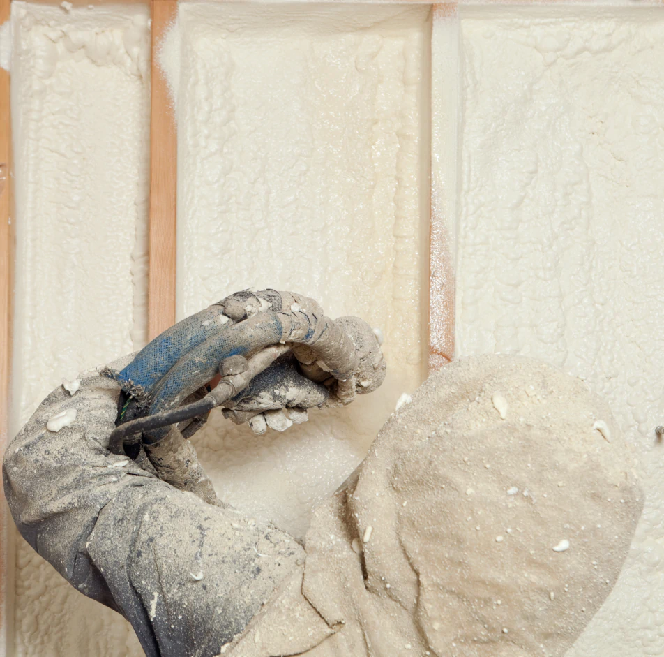 worker spraying expandable foam insulation between wall studs